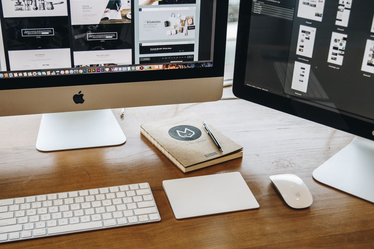 A clean desk arrangement with two monitors, a keyboard, mouse, and notebook designed for productivity.